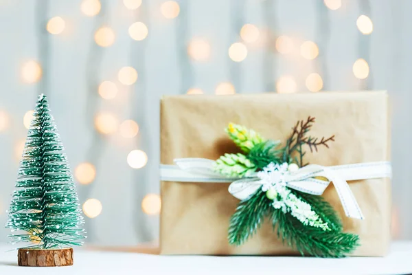 Un árbol de Navidad con caja de regalo sobre fondo borroso de banner bokeh de una guirnalda luminosa y pizarras blancas. Feliz Navidad, ideas para postales para vacaciones de invierno — Foto de Stock