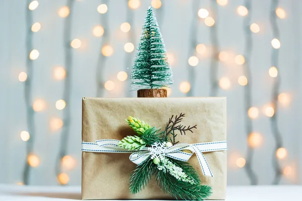 Een kerstboom met de doos van de gift op wazig bokeh banner achtergrond van een lichtgevende garlandh en witte planken. Vrolijke Kerstmis, ideeën voor ansichtkaarten voor wintervakantie — Stockfoto