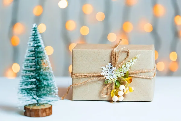 Un árbol de Navidad con caja de regalo sobre fondo borroso de banner bokeh de una guirnalda luminosa y pizarras blancas. Feliz Navidad, ideas para postales para vacaciones de invierno — Foto de Stock