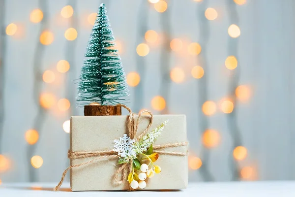 Un árbol de Navidad con caja de regalo sobre fondo borroso de banner bokeh de una guirnalda luminosa y pizarras blancas. Feliz Navidad, ideas para postales para vacaciones de invierno — Foto de Stock