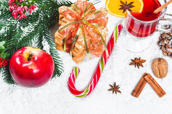 Copa de Navidad de vino tinto con especias en la mesa con palos de canela, ramas de árbol de Navidad, nieve, pan de jengibre, cono, dulces, decoraciones de Año Nuevo sobre fondo de madera blanca. Espacio libre —  Fotos de Stock