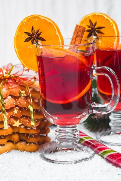 Bicchiere natalizio di vin brulè rosso su tavola con bastoncini di cannella, rami di albero di Natale, neve, pan di zenzero, cono, caramelle, decorazioni di Capodanno su sfondo bianco in legno. Spazio libero — Foto Stock