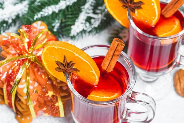 Bicchiere natalizio di vin brulè rosso su tavola con bastoncini di cannella, rami di albero di Natale, neve, pan di zenzero, cono, caramelle, decorazioni di Capodanno su sfondo bianco in legno. Spazio libero — Foto Stock