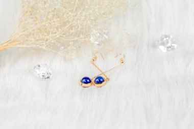 Mavi yuvarlak boncuklardan ve altın sarısı metalden yapılmış küpeler. Solmuş bitkiler ve şeffaf buz küpleri fotoğrafçılık için iyi dekorasyonlardır. Beyaz peluş battaniye.