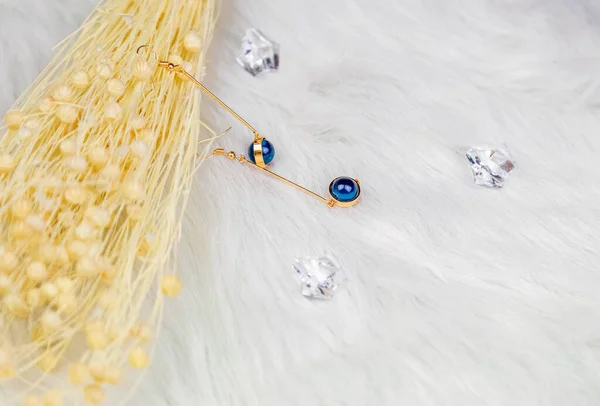 耳环由蓝色圆形珠子和金黄色金属制成 以黄色干草本植物为背景 枯萎的植物和透明的冰块是很好的摄影装饰 白色毛毯 — 图库照片