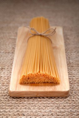İtalyan spagetti makarnası, doğal ahşap tabakta uzanan halatla bağlanmış.