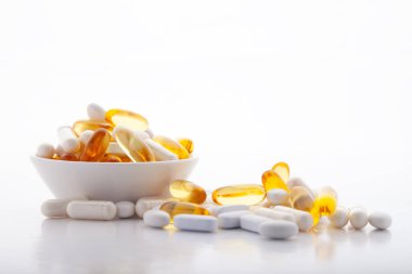 Çeşitli ilaçlar ilaç vitaminleri, haplar, gri arka planda kasede uyuşturucular. Beyaz gıda besin takviyesi sert kabuklu kapsüller toz, somon yağı softgel Omega 3