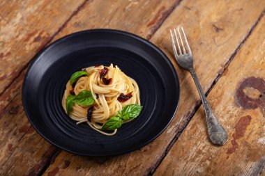 Geleneksel İtalyan yemeği, sebzeli spagetti makarna, biber, fesleğen yaprakları kahverengi kırsal çatal üzerinde siyah yuvarlak yaprak, ahşap arka plan. Yemek tasarımcısını kabul et