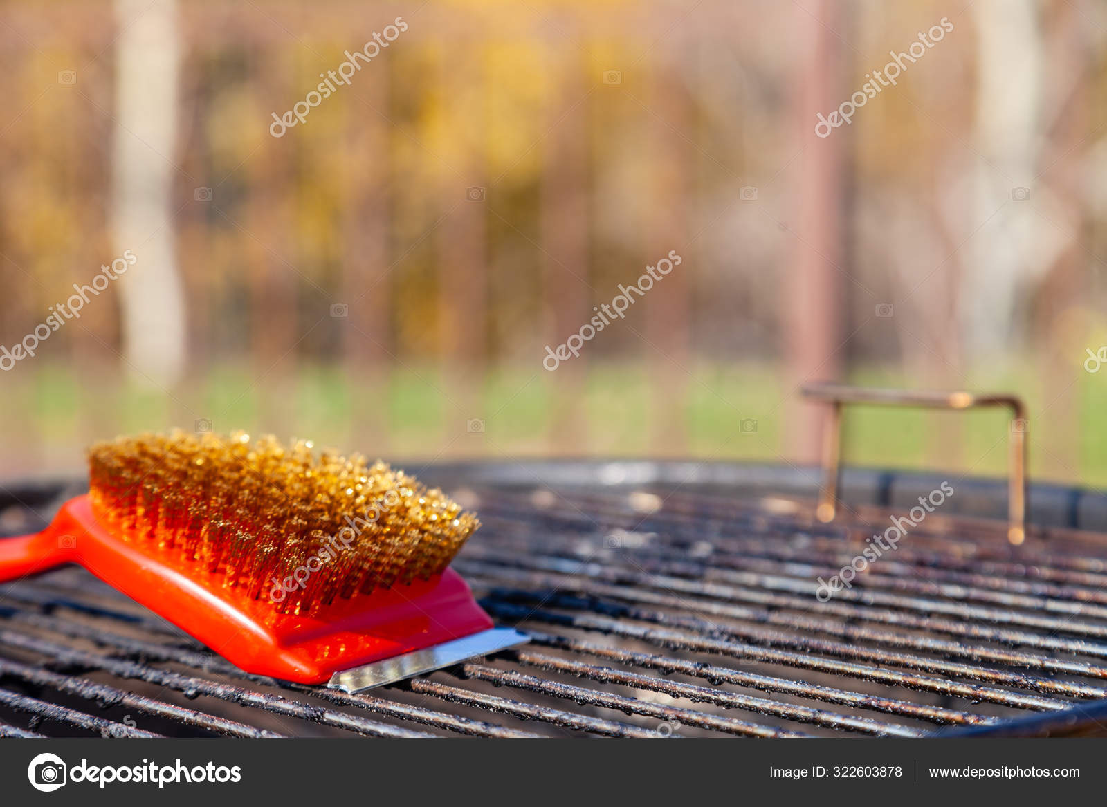 Close-up of a red brush with golden bristles and a scraper for cleaning a barbecue  grill grate. The concept of cleaning after lunch in open air, picnic,  barbecue, lunch Stock Photo by ©