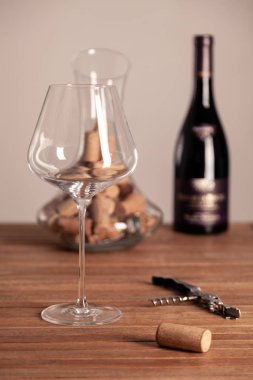 Kristal kırmızı şarap kadehi, şişe, tirbuşon, açacağı, şarap bıçağı, şeffaf sürahi, ahşap masa mantarları. Yakın çekim, dikey, seçici odaklanma, yan görüş. Şarap mahzenindeki deguasyon kavramını kabul et