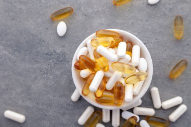 Çeşitli ilaçlar ilaç vitaminleri, haplar, gri arka planda kasede uyuşturucular. Beyaz gıda besin takviyesi sert kabuklu kapsüller toz, somon yağı softgel Omega 3