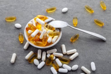 Dağınık ilaç vitaminleri, haplar, kasede gri arka planda metal kaşık olan ilaçlar. Beyaz gıda besin takviyesi sert kabuklu kapsüller toz, somon yağı softgel Omega 3