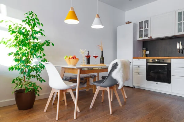 Moderne kjøkken, spisestue, hvite møbler, lamper, trebord, rødvin, glass. Dekor, design, reklame, kreditt, boliglån, familiebolig, magasinforside – stockfoto