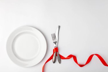 Beyaz arka planda romantik şenlik masası. Sevgililer Günü kartı şablonu. Kırmızı kurdele, tabak, çatal, çatal, bıçak. Kavram yıldönümü, doğum günü, metin yeri, telif alanı, üst görünüm