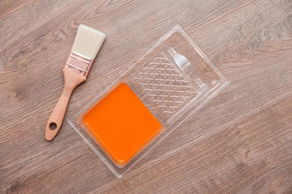 Närbild målare cuvette med orange färg på trä brunt golv. Högst upp. Begreppsfärgad ljus kreativ inredning för ung familj. Hur man målar träytan — Stockfoto