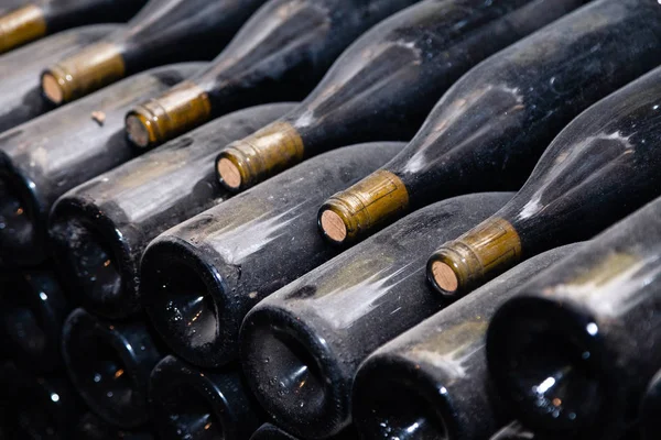 Garrafas de vinho empoeiradas escuras antigas que envelhecem em adega subterrânea em fileiras. Conceito abóbada adega com vinhos raros, coleção exclusiva. Pilhas de garrafas de vinho descansando, deitado em prateleiras em caverna velha — Fotografia de Stock