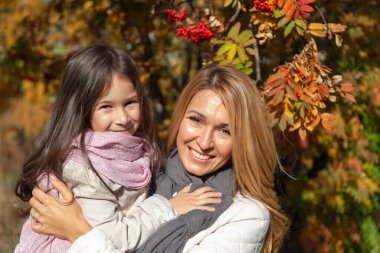 Güzel anne, sonbahar ormanında kızını kucaklıyor.