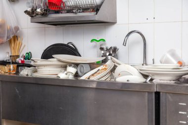 Kirli bulaşık, çanak çömlek, sofra takımı dolu bir metal lavabo.