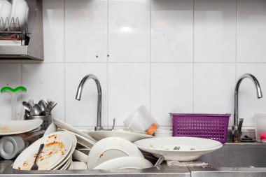 Kirli bulaşık, çanak çömlek, sofra takımı dolu bir metal lavabo.