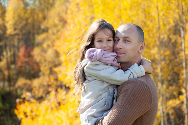 dad hugs daughter in sunny autumn forest