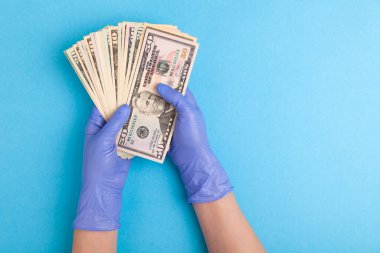 Lateks mor eldivenli eller mavi arka planda dolar banknotları tutar
