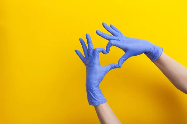 Female hand in lilac glove, fingers folded into a heart sign on yellow background — Stock Photo, Image