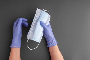 Lastik eldivenli kadın elleri tek kullanımlık maskeyi tutuyor.