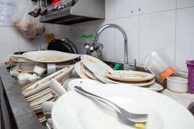 Kirli bulaşık, çanak çömlek, sofra takımı dolu bir metal lavabo.