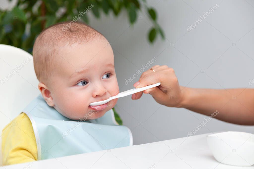 Little baby boy in color clothes eating yoghurt from spoon, dirty mouth