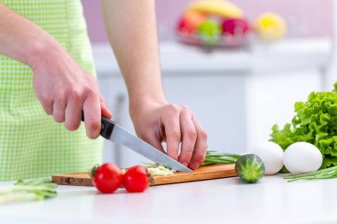 Önlüklü bir aşçı kadın evdeki mutfakta taze sağlıklı sebze salatası için çevre dostu ürünler doğruyor. Diyet ve temiz yemek. Sebze yemekleri için hazırlık