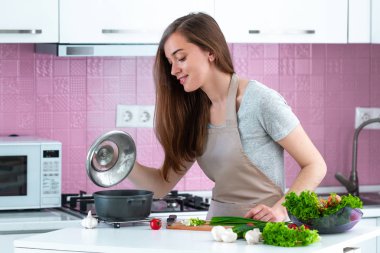 Önlüklü kadın mutfakta taze olgun sebzelerden yemek pişiriyor. Temiz yemek ve sağlıklı yaşam tarzı. 
