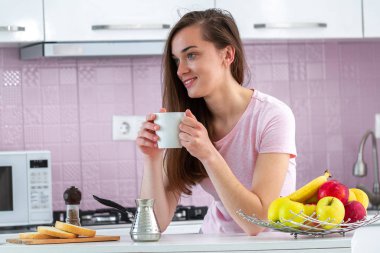 Genç, çekici, kadın sabahın erken saatlerinde mutfakta kahvaltıda sıcak, lezzetli kahve içiyor. Yeni güne başla