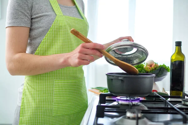 Cooking woman in apron standing near stove and cooking soup for dinner. Clean healthy food and proper nutrition. Diet