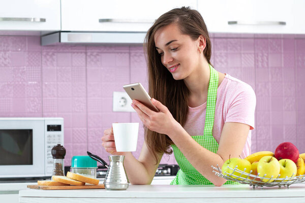 Happy, attractive, woman chatting online and drinking hot, tasty coffee for breakfast in early morning at kitchen at home. Online, phone addiction 