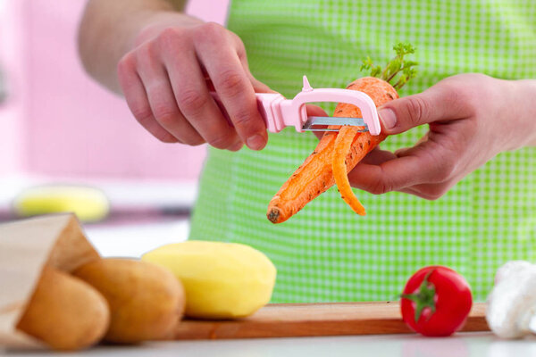 Housewife in apron peeling ripe carrot with a peeler for cooking fresh vegetable dishes and salads. Proper healthy eating and clean food 