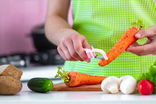Peeling ripe carrot with a peeler for cooking fresh vegetable dishes and salads. Proper healthy eating and clean food 
