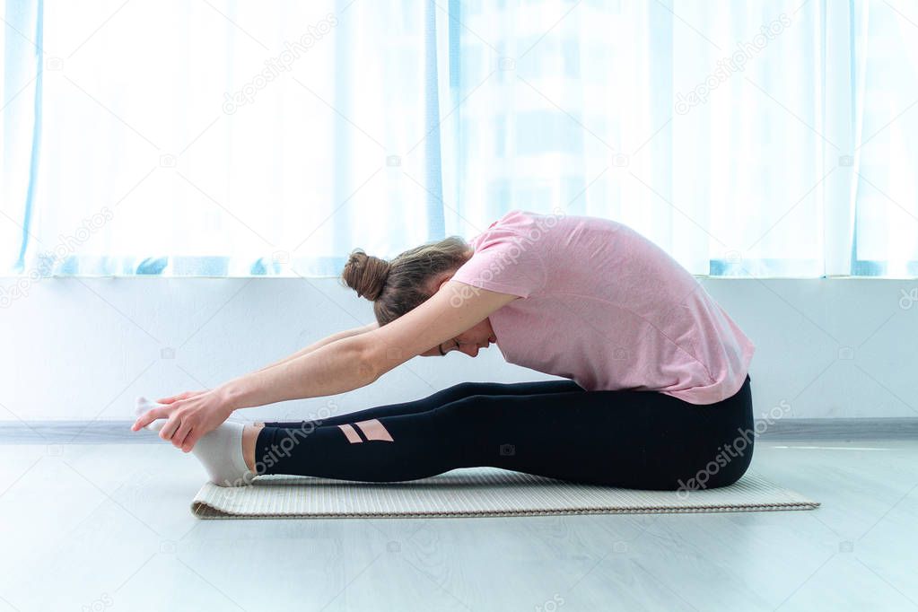 Young woman forward bends, do stretching the muscles and fitness exercises on yoga mat at home. Lose weight and keep fit. Healthy sports lifestyle 
