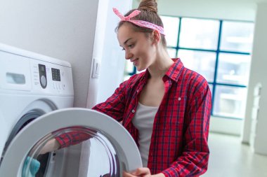 Mutlu ev hanımı evde çamaşır makinesine çamaşır yüklüyor. 