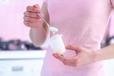 Elinde yoğurt kasesi ve yoğurt kaşığı olan kadın evdeki mutfağı kapatıyor. 