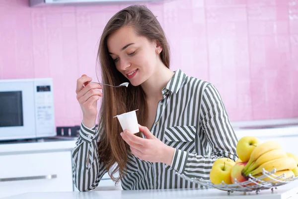 一个年轻的 微笑的 快乐的女人在厨房吃酸奶当早餐的画像 — 图库照片