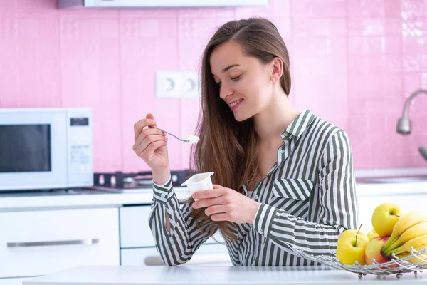 一个年轻的 微笑的 快乐的女人在厨房里端着酸奶杯 在家里吃新鲜的酸奶当点心的画像 — 图库照片
