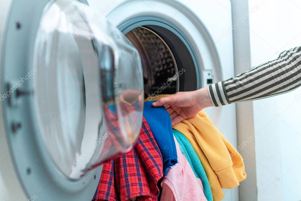 Loading colored clothes and linen in washing machine. Doing laundry at home 