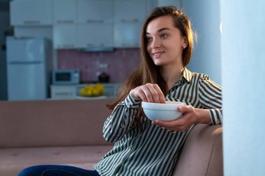 Genç ve çekici bir kadının portresi patlamış mısır yiyor ve evde tek başına televizyon izliyor. 
