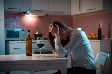 Mutsuz, yalnız, stresli, kırmızı şaraplı kadın akşamları mutfakta tek başına içiyor. Hayat zorlukları ve sorunlar. Kadın alkolizmi ve alkol bağımlılığı