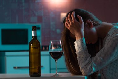 Mutsuz, yalnız, stresli, kırmızı şaraplı kadın akşamları mutfakta tek başına içiyor. Hayat zorlukları ve sorunlar. Kadın alkolizmi ve alkol bağımlılığı