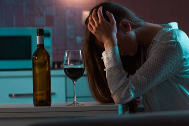 Mutsuz, yalnız, stresli, kırmızı şaraplı kadın akşamları mutfakta tek başına içiyor. Hayat zorlukları ve sorunlar. Kadın alkolizmi ve alkol bağımlılığı