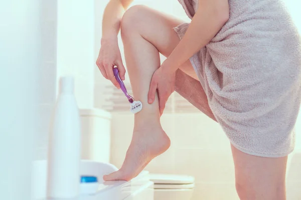 タオルの女性はシェーバーを使用してバスルームで足を剃る 滑らかな肌 家庭での美容と衛生の治療 — ストック写真