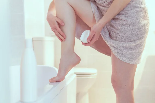 バスルームで足を剃った後 乾燥肌のための保湿と栄養クリームを適用タオルの女性 ホームでの滑らかな肌 化粧品や美容トリートメント — ストック写真