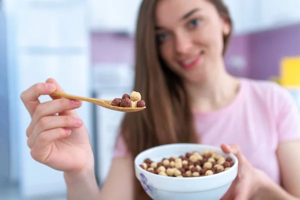 年轻的 面带微笑的美丽的黑发女子 手里拿着盛满巧克力球的麦片勺和麦片碗在家里吃早餐 — 图库照片