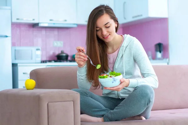 Young happy vegan woman eating vegetable salad for lunch at home. Diet and fitness eating. Clean and healthy food